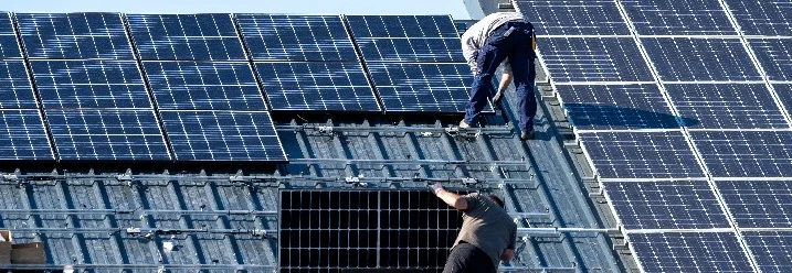Zwei Personen montieren Solarmodule auf einem Dach.